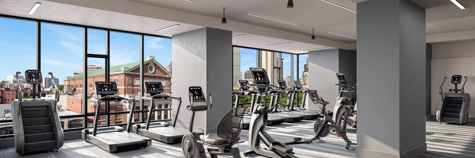 Bright fitness center with cardio equipment and large windows overlooking city